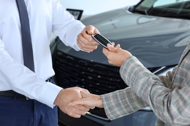 Photo of Salesman giving key to client near new car in salon, closeup