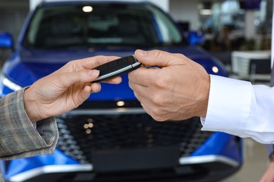 Photo of Saleswoman giving key to client near new car in salon, closeup