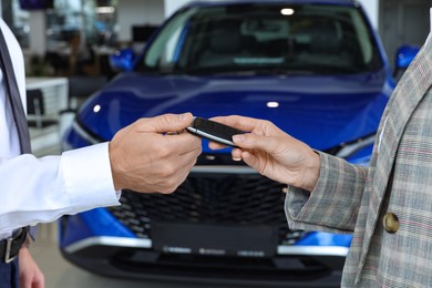 Photo of Saleswoman giving key to client near new car in salon, closeup