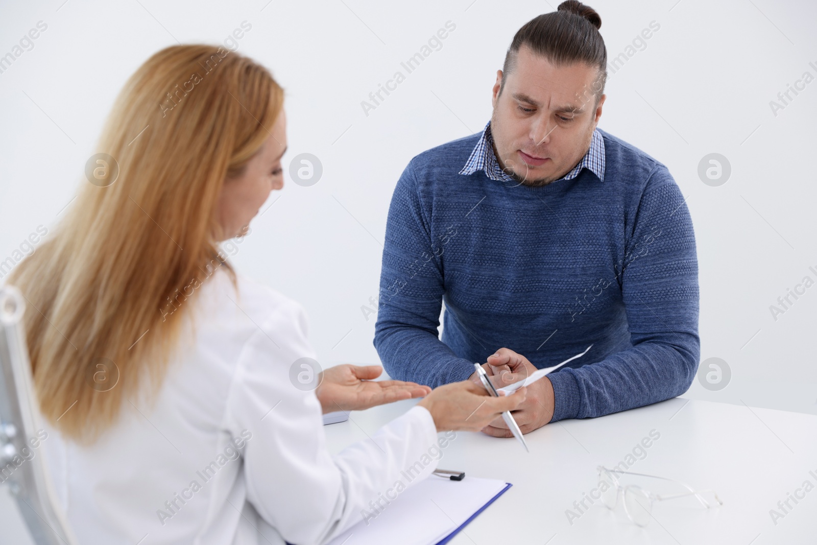 Photo of Nutritionist consulting overweight man at table in clinic