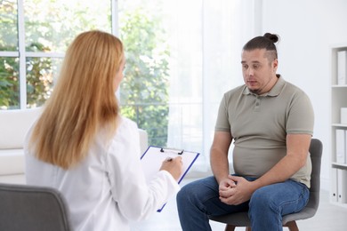 Photo of Nutritionist with clipboard consulting overweight man in clinic