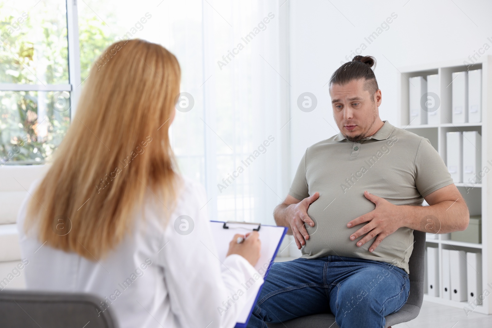 Photo of Nutritionist with clipboard consulting overweight man in clinic