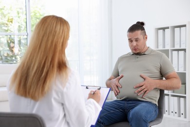 Nutritionist with clipboard consulting overweight man in clinic