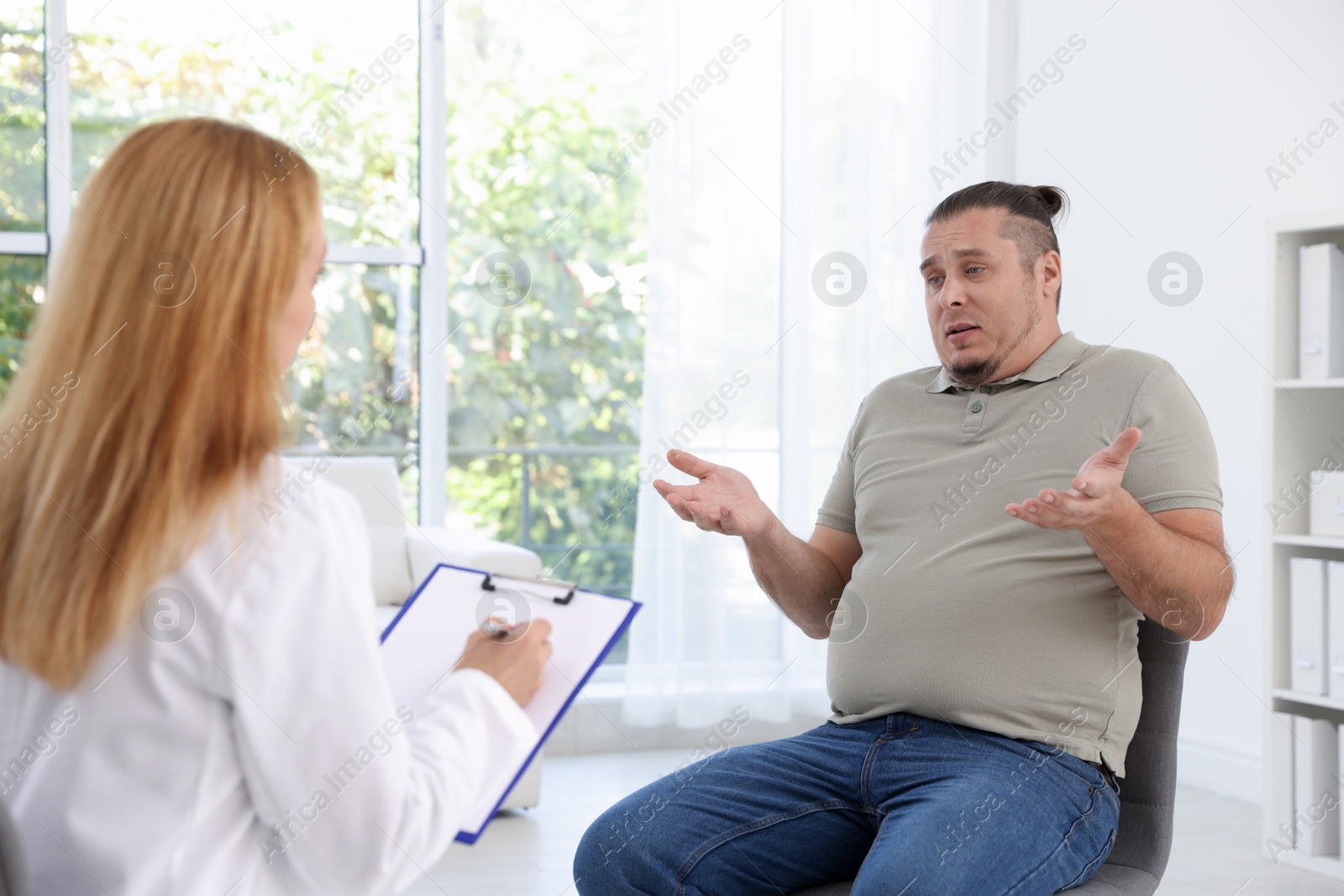 Photo of Nutritionist with clipboard consulting overweight man in clinic