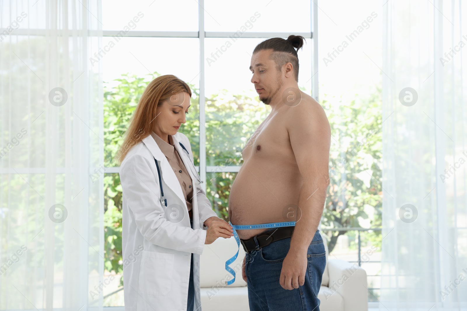 Photo of Nutritionist measuring overweight man's waist with tape in clinic