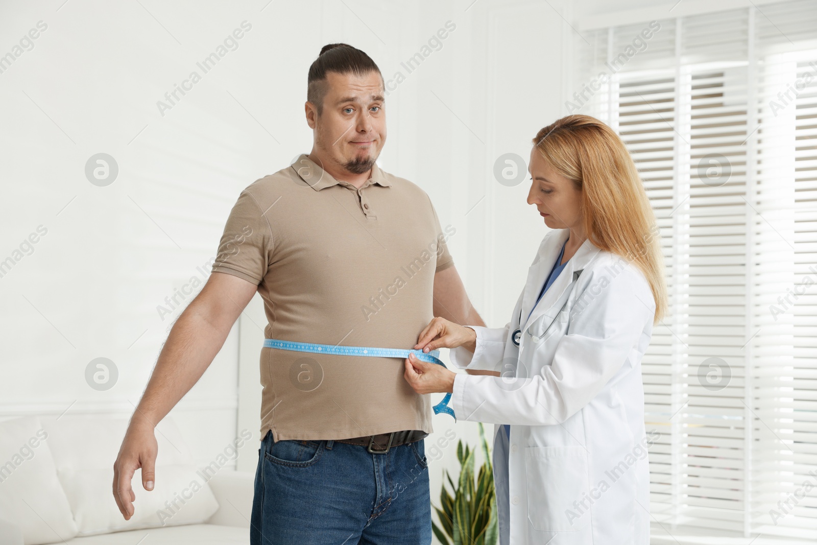 Photo of Nutritionist measuring overweight man's waist with tape in clinic