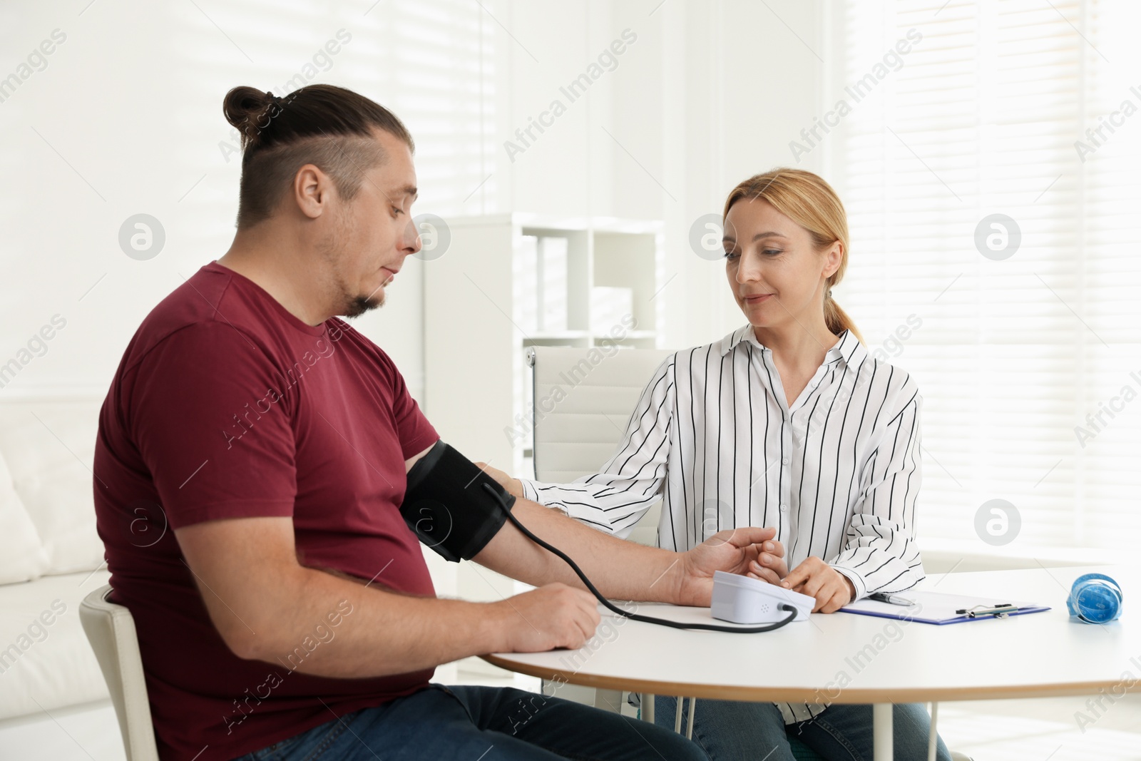 Photo of Nutritionist measuring overweight patient's blood pressure at table in clinic