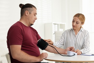 Photo of Nutritionist measuring overweight patient's blood pressure at table in clinic