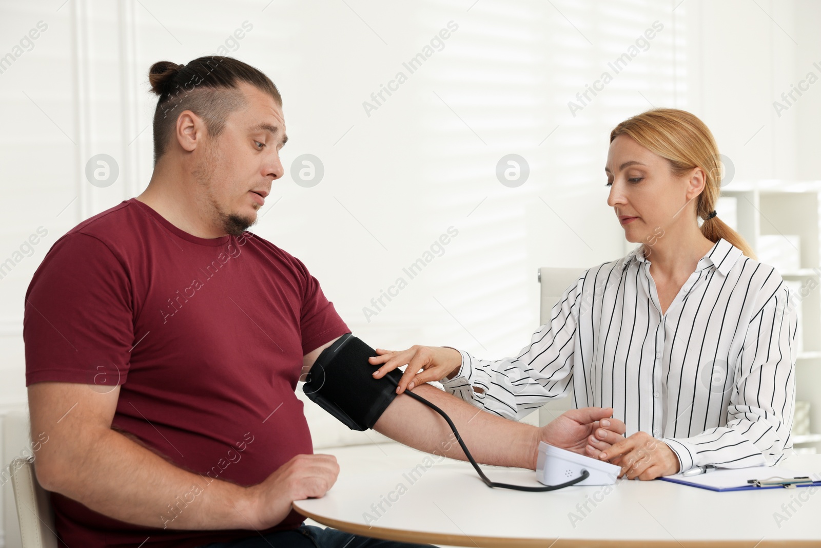 Photo of Nutritionist measuring overweight patient's blood pressure at table in clinic