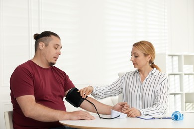 Photo of Nutritionist measuring overweight patient's blood pressure at table in clinic