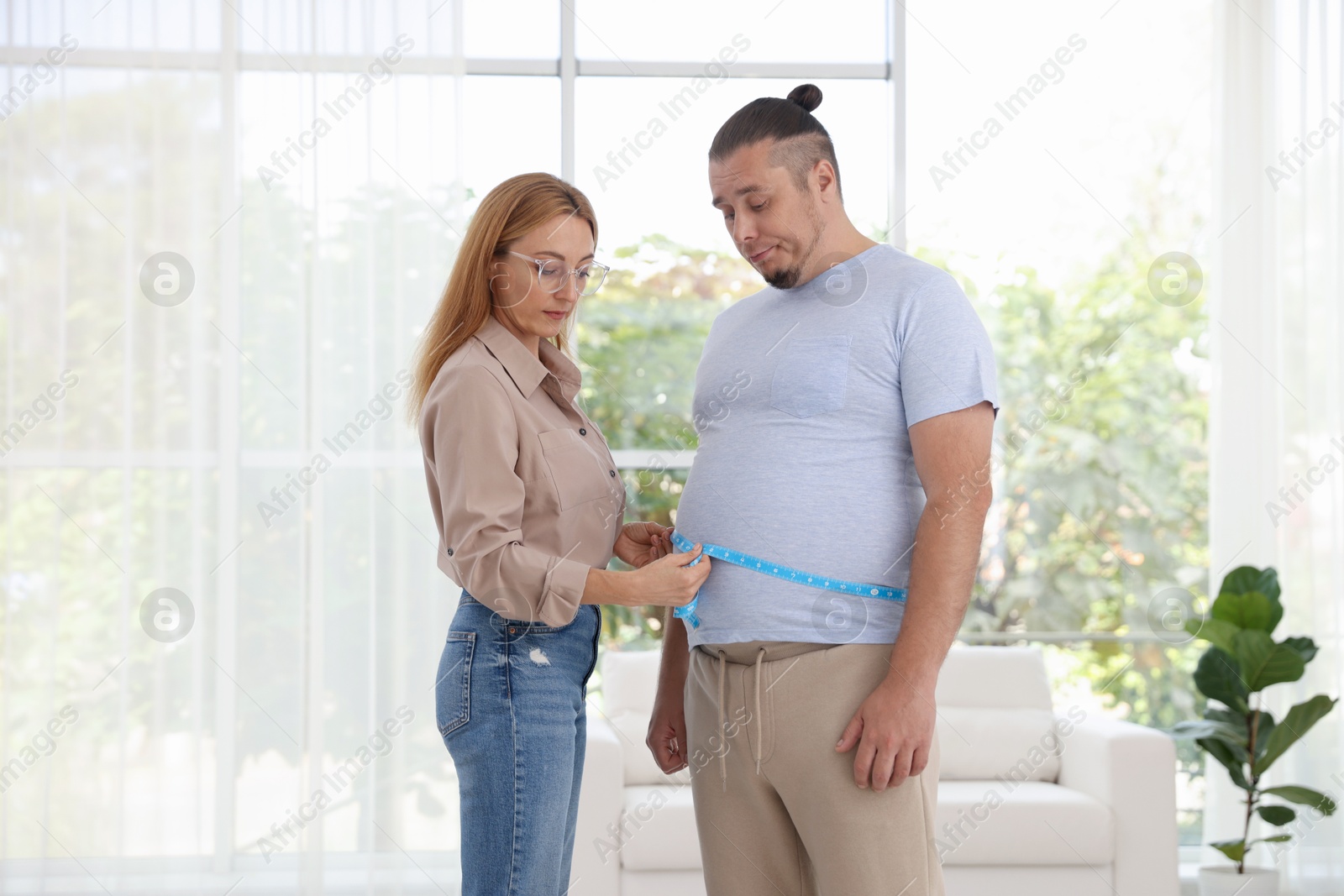 Photo of Nutritionist measuring overweight man's waist with tape in clinic