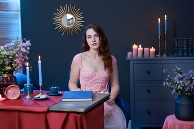 Photo of Beautiful young woman sitting at table in room. Fashion vintage style portrait