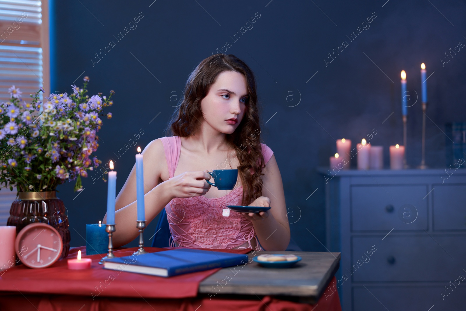 Photo of Beautiful young woman with cup of tea at table in room. Fashion vintage style portrait