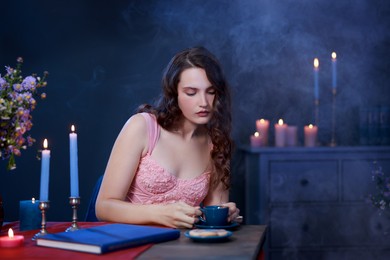 Beautiful young woman with cup of tea at table in room. Fashion vintage style portrait