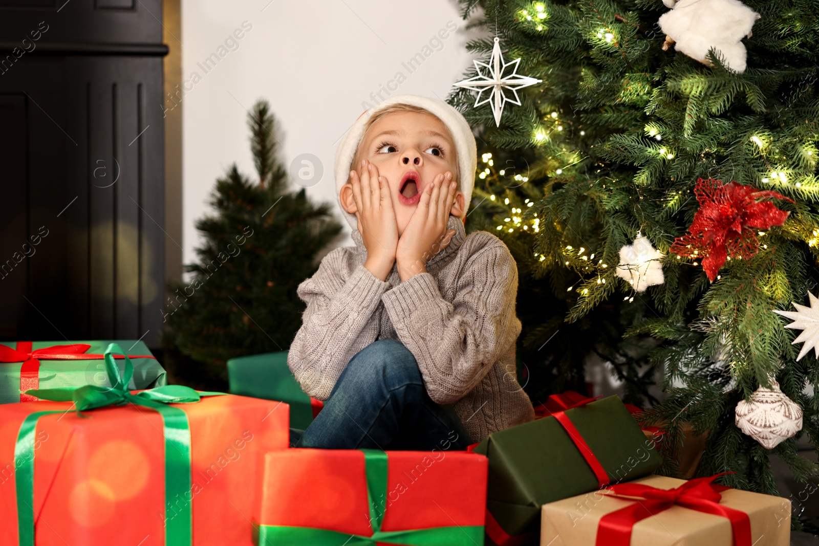 Photo of Little boy in Santa hat with Christmas gifts at home