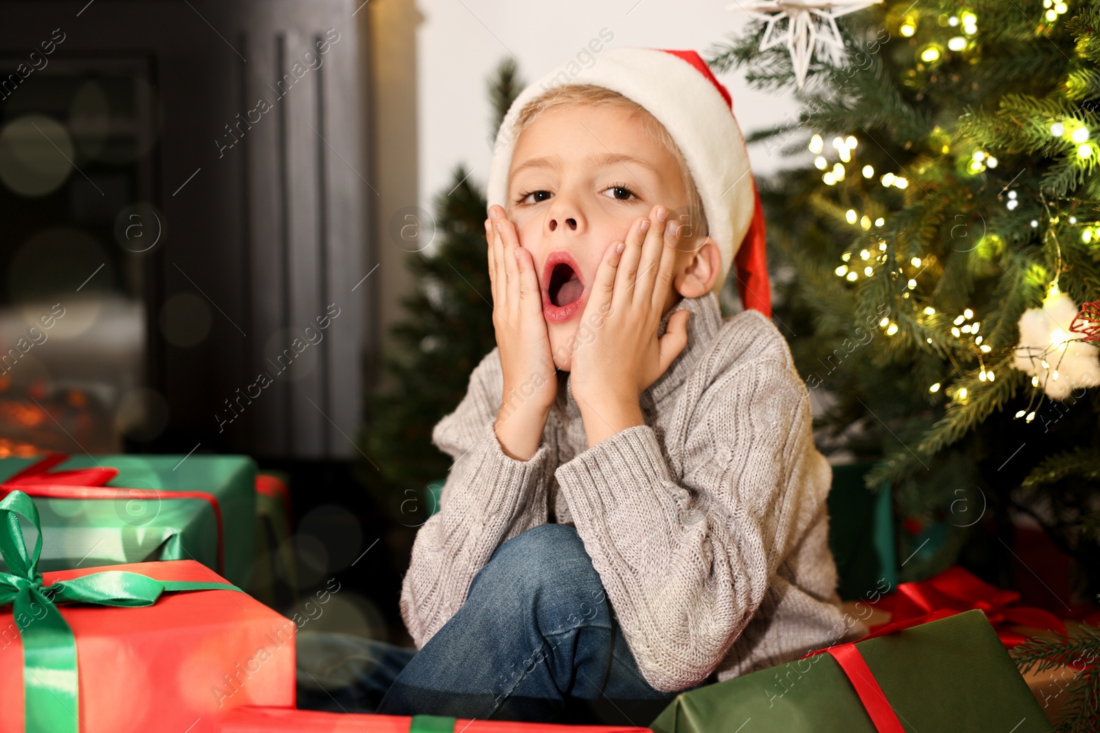 Photo of Little boy in Santa hat with Christmas gifts at home