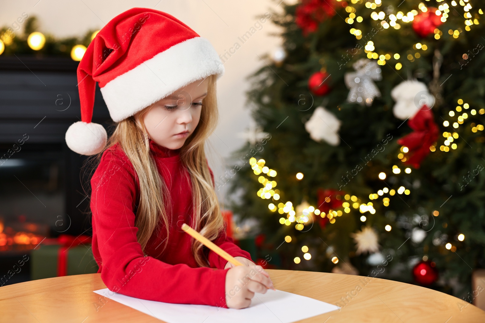 Photo of Little girl writing letter to Santa Claus at table indoors. Christmas celebration