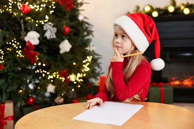 Photo of Little girl writing letter to Santa Claus at table indoors. Christmas celebration