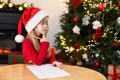 Photo of Little girl writing letter to Santa Claus at table indoors. Christmas celebration