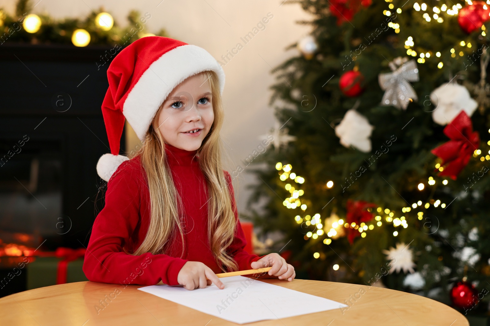 Photo of Little girl writing letter to Santa Claus at table indoors. Christmas celebration