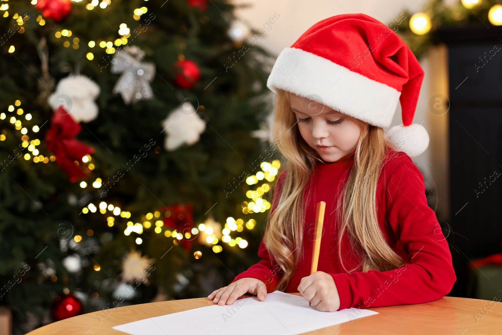 Photo of Little girl writing letter to Santa Claus at table indoors. Christmas celebration