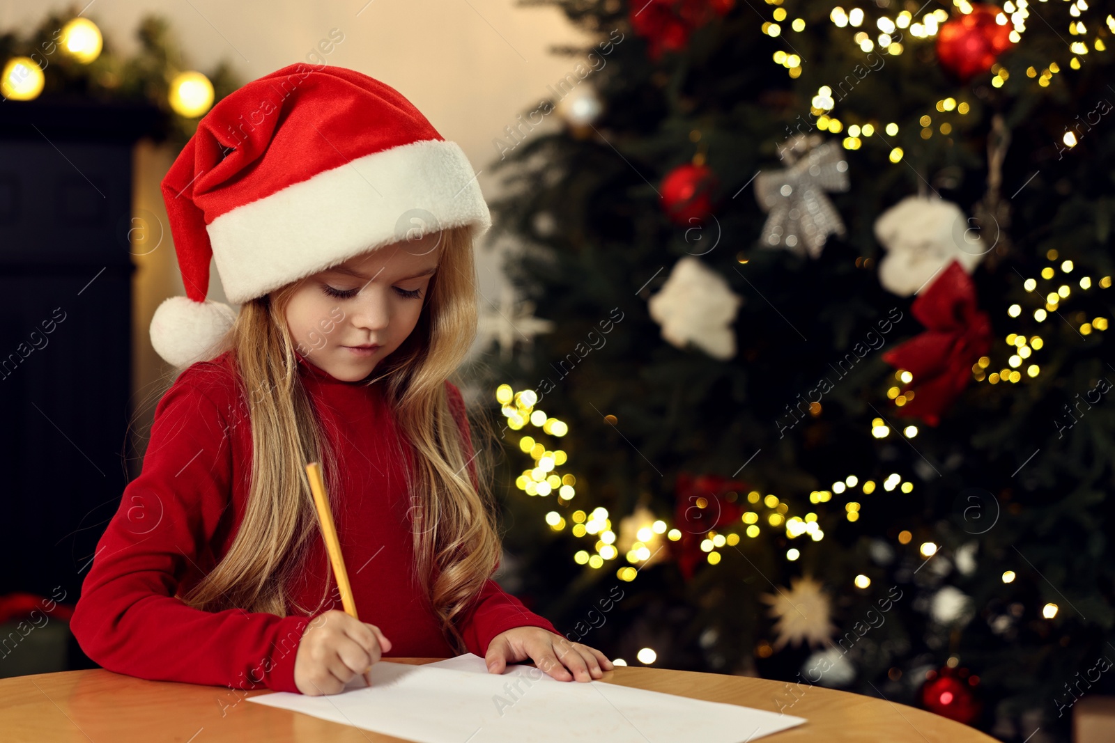 Photo of Little girl writing letter to Santa Claus at table indoors. Christmas celebration