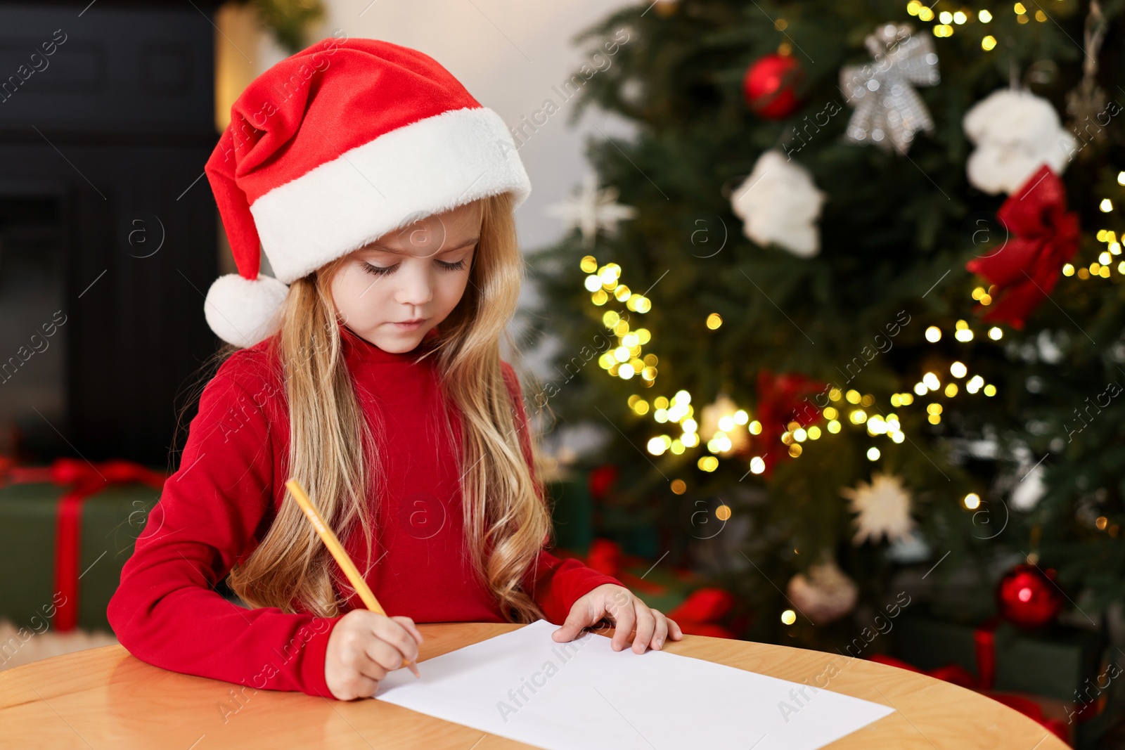 Photo of Little girl writing letter to Santa Claus at table indoors. Christmas celebration