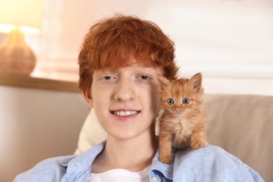 Redhead teenage boy with cute ginger kitten on sofa indoors