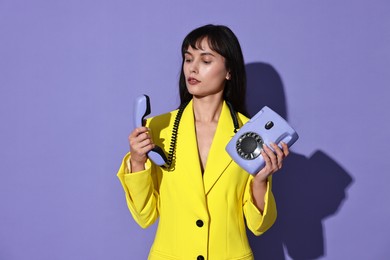 Woman in yellow jacket with corded telephone on purple background