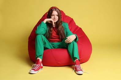 Photo of Teenage red-haired girl with headphones sitting on beanbag against golden background