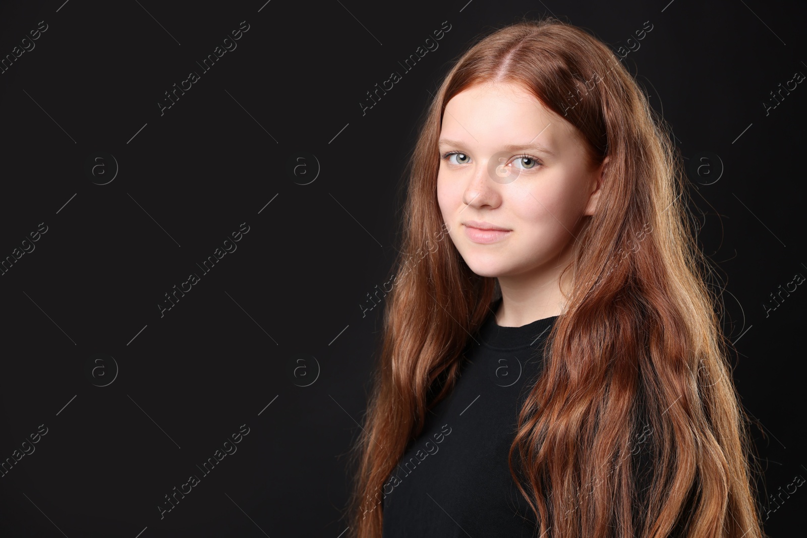 Photo of Pretty red-haired teenage girl on black background. Space for text