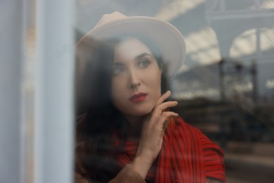 Photo of Woman with red scarf at railway station, view through glass window