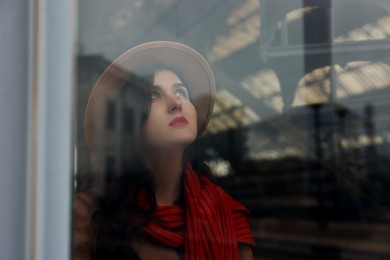 Photo of Woman with red scarf at railway station, view through glass window, space for text