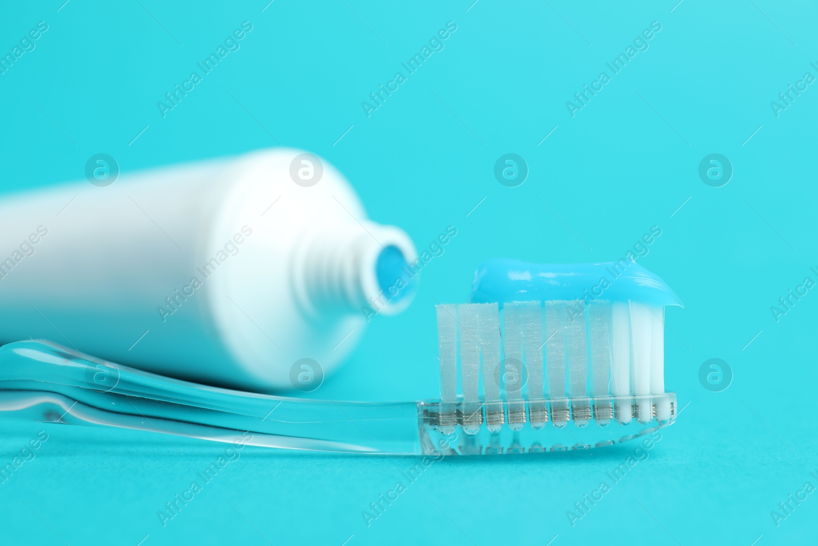 Photo of Toothbrush with toothpaste and tube on light blue background, closeup