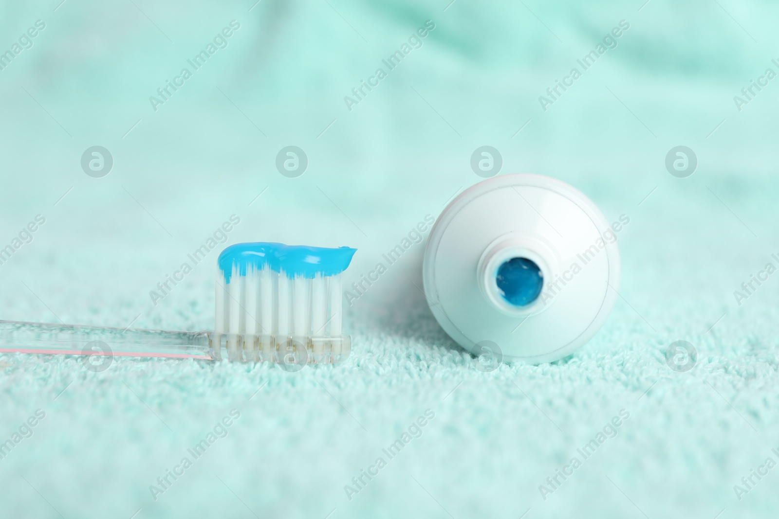 Photo of Toothbrush with toothpaste and tube on turquoise towel, closeup