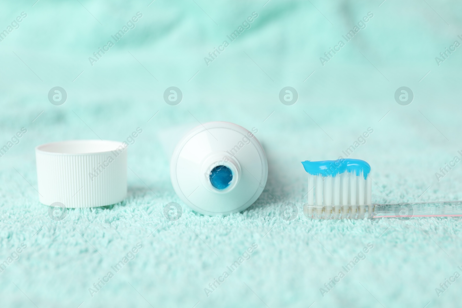 Photo of Toothbrush with toothpaste and tube on turquoise towel, closeup