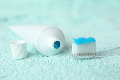 Toothbrush with toothpaste and tube on turquoise towel, closeup