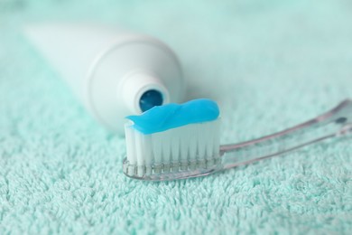 Photo of Toothbrush with toothpaste and tube on turquoise towel, closeup