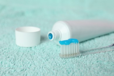 Photo of Toothbrush with toothpaste and tube on turquoise towel, closeup