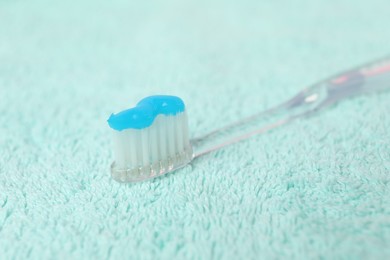 Photo of Toothbrush with toothpaste on turquoise towel, closeup