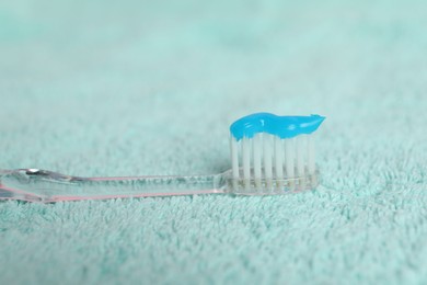 Photo of Toothbrush with toothpaste on turquoise towel, closeup