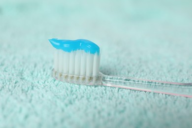 Photo of Toothbrush with toothpaste on turquoise towel, closeup