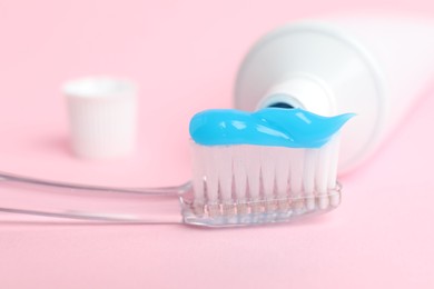 Photo of Toothbrush with toothpaste and tube on pink background, closeup