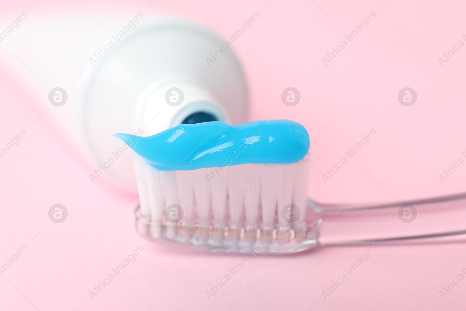 Photo of Toothbrush with toothpaste and tube on pink background, closeup