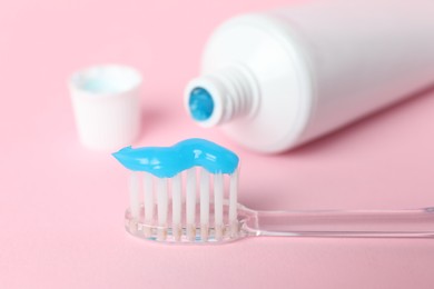 Photo of Toothbrush with toothpaste and tube on pink background, closeup