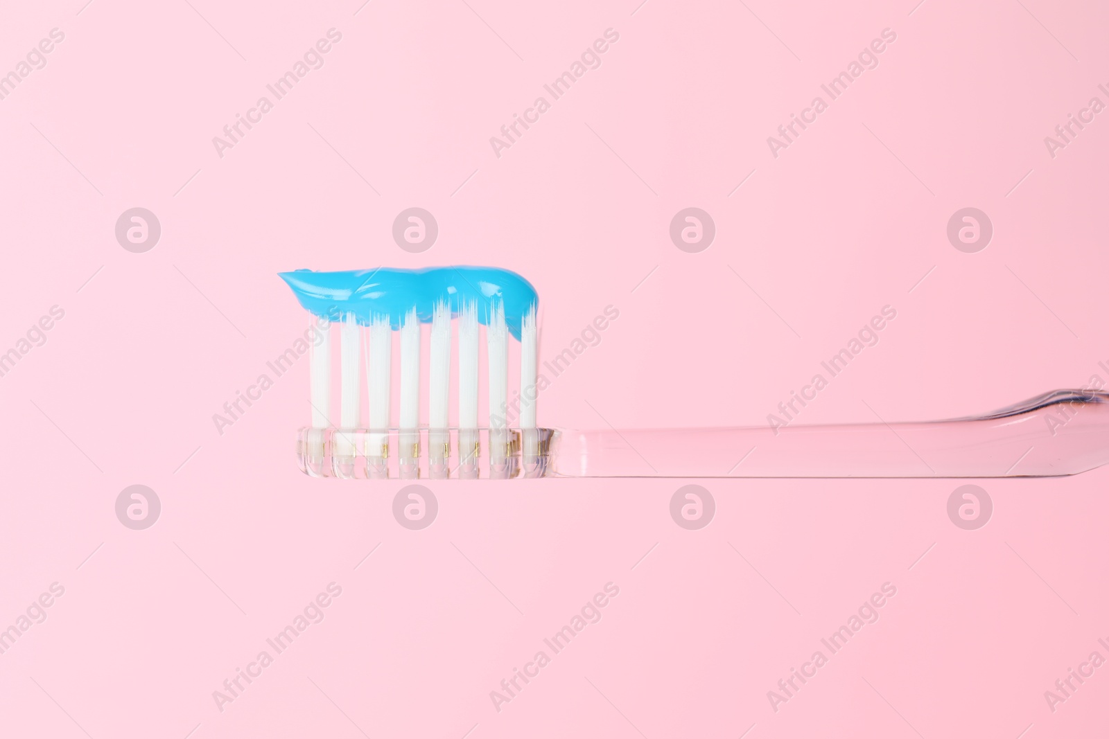 Photo of Toothbrush with toothpaste in air on pink background, closeup