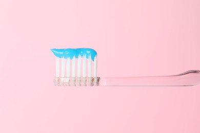 Photo of Toothbrush with toothpaste in air on pink background, closeup