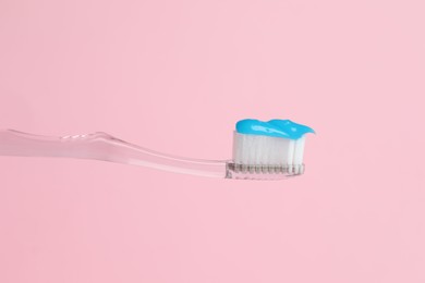 Photo of Toothbrush with toothpaste in air on pink background, closeup