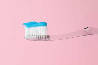 Photo of Toothbrush with toothpaste in air on pink background, closeup