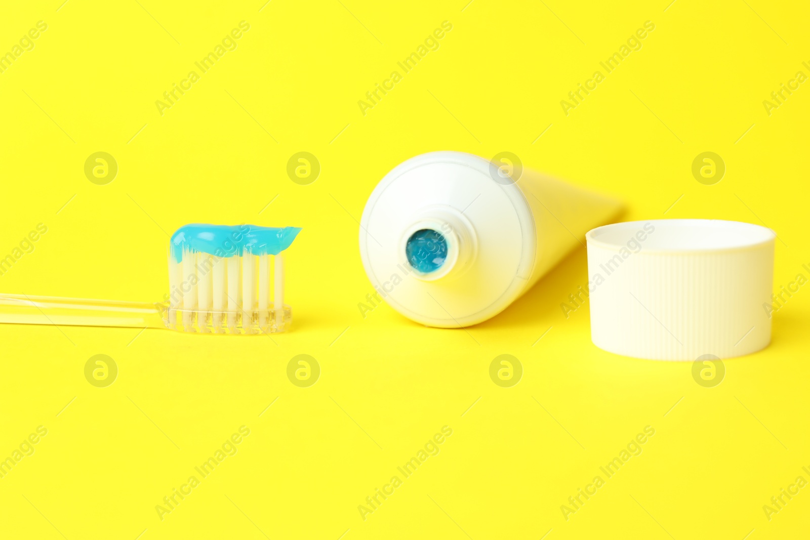 Photo of Toothbrush with toothpaste and tube on yellow background, closeup